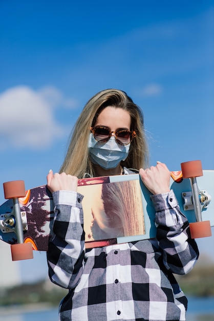 Ritratto di una giovane donna in una maschera medica con longboard