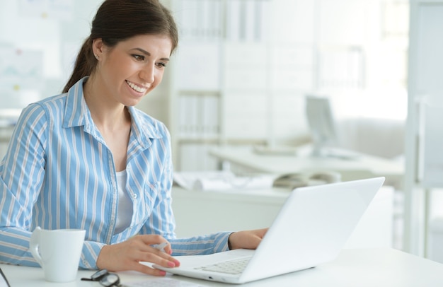 Portrait of a young female office worker, using laptop