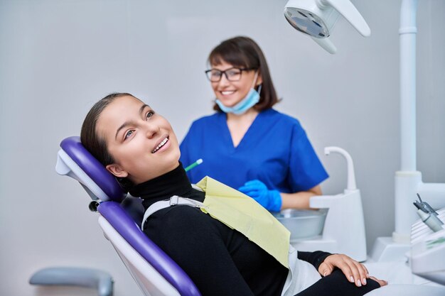 치과 의사와 함께 치과 의자에 앉아있는 카메라를 바라보는 한 미소를 가진 젊은 여성 환자의 초상화 치과 위생 치료 치과 건강 관리 개념