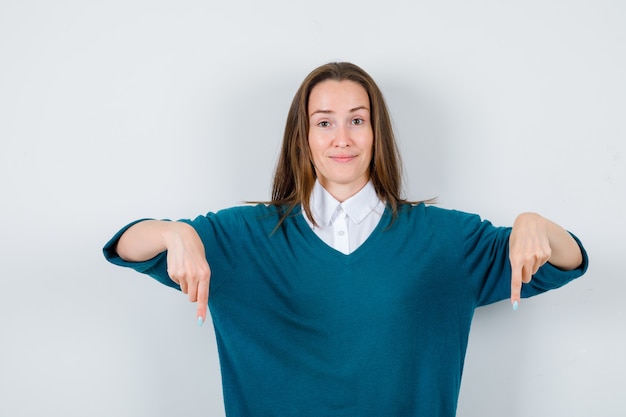 Foto ritratto di giovane donna che punta verso il basso con un maglione sopra la maglietta e guarda una vista frontale allegra