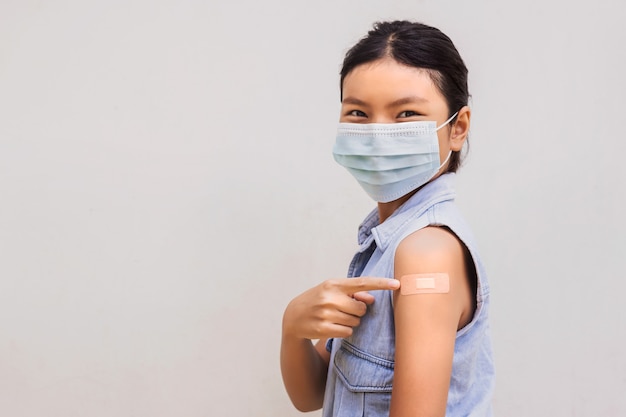 Portrait of a young female pointing plaster on arm after getting a vaccine. standing on white background