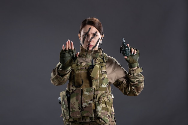 Portrait of young female soldier with grenade on her hands dark wall