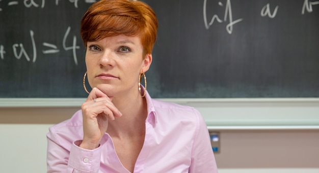 Portrait of young female teacher at school lesson with blackboard