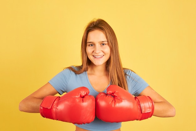 Portrait of young fighter woman wearing red boxing gloves on yellow background