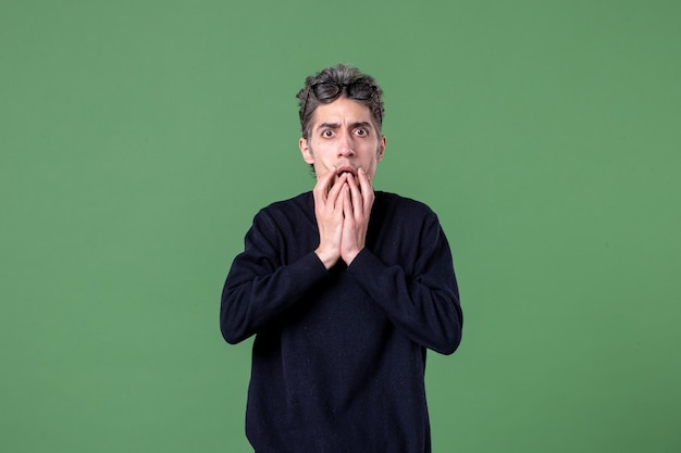 Portrait of young genius man dressed casually with surprised expression in studio shot on green wall