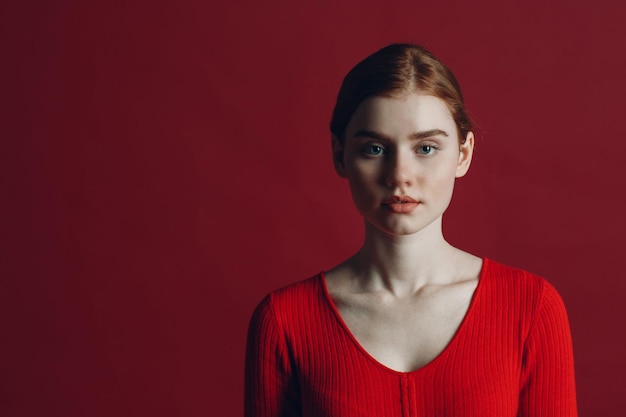 Портрет молодой рыжей серьезной женщины на красном фоне