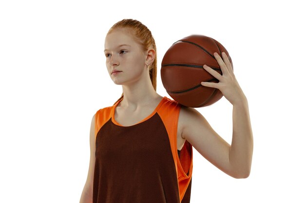 흰색 스튜디오 배경 위에 절연 공을 들고 포즈를 취하는 어린 소녀 농구 선수의 초상화