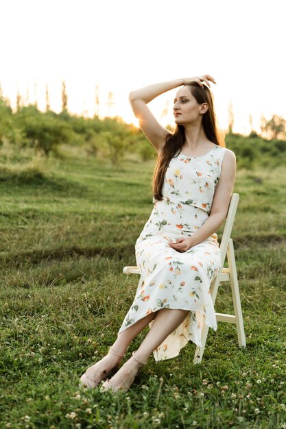 Portrait of a young girl in a beautiful dress sitting on a chair in nature.