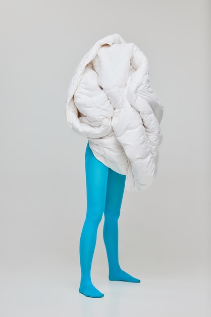 Photo portrait of young girl in blue tights covered in white blanket isolated over grey studio background