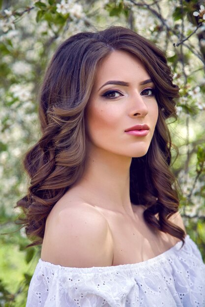 Photo portrait of a young girl brown hair with make-up in the cherry sakura pink ,white in a white dress