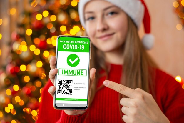 Portrait of a young girl in Christmas hat with digital vaccination certificate in her phone Coronavirus vaccination concept