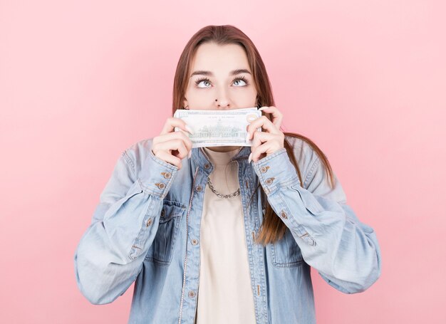 Ritratto di una giovane ragazza in camicia di jeans odorando un pacchetto di dollari.