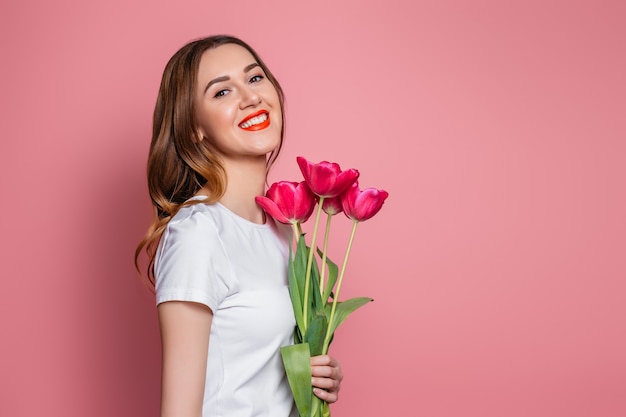 Portrait of a young girl holding a bouquet of tulips and smiling isolated on a pink background 