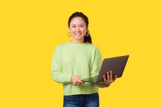 Portrait of a young girl holding a computer on yellow.