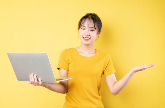 Portrait of young girl holding laptop in hand on yellow background