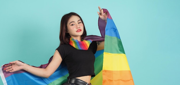 Portrait of young girl holding an LGBT flag standing against a blue green background studio