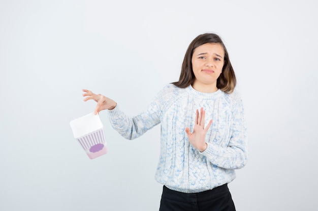 Portrait of young girl in knitted sweater showing empty popcorn box. 