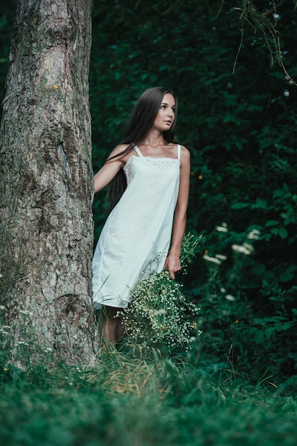 Photo portrait of a young girl near a tree with white flowers in hands