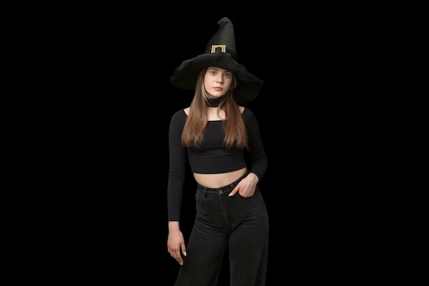 Ritratto di giovane ragazza con cappello da strega appuntito e vestiti neri è isolato su sfondo nero copia spazio costume di halloween