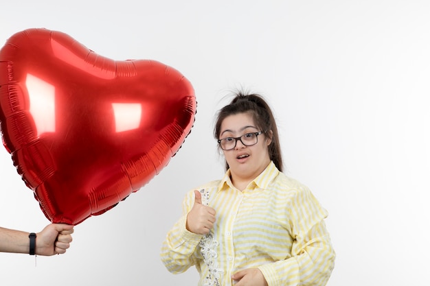 Portrait of young girl showing thumb up and standing near air balloon in shape of heart