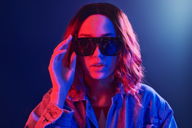 Portrait of young girl in sunglasses in red and blue neon in studio