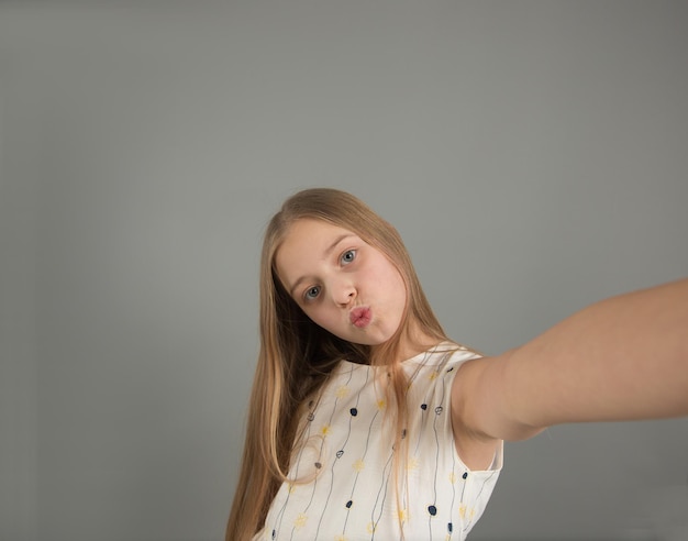 Портрет молодой девушки, делающей селфи с протянутой рукой на сером фоне