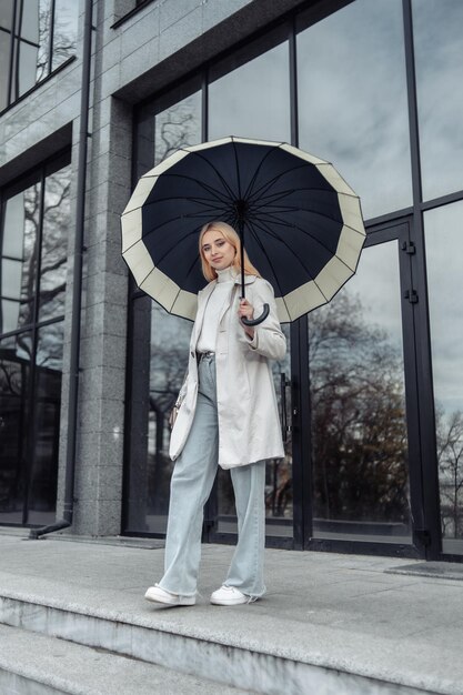 Portrait of young girl in trench coat with umbrella near the business center