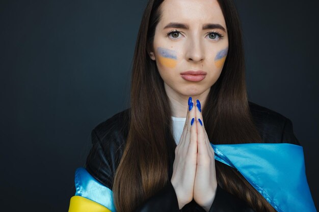 Portrait of young girl with blue and yellow ukrainian flag on her cheek on black background