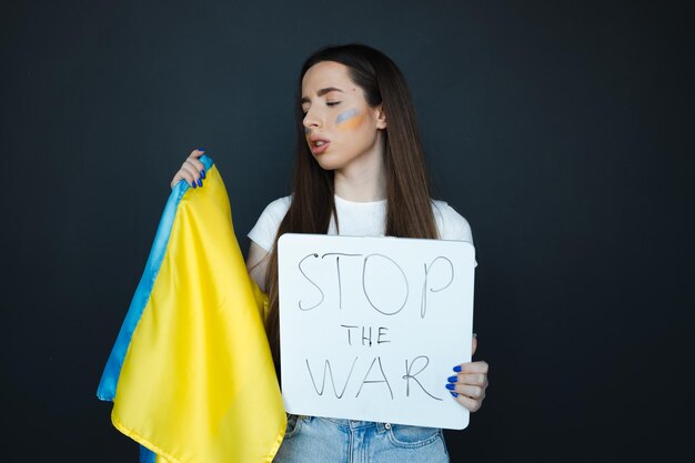 Portrait of young girl with blue and yellow ukrainian flag on her cheek on black background