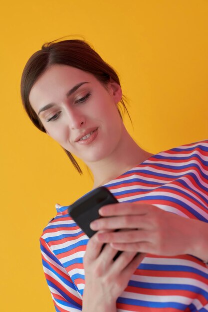 Portrait of young girl with happy face while using smartphone
isolated on pink background. female model smiling while chatting or
browsing on social networks. fashion and technology concept