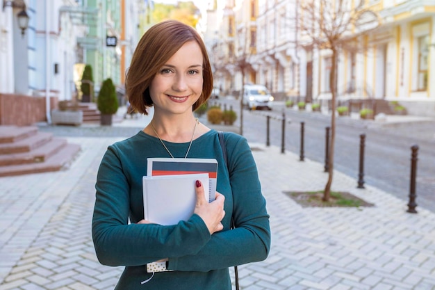 Portrait of a young girl with textbooks in her hands and looking at the camera on a city street.