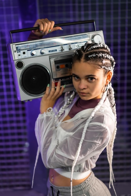 Portrait of a young girl with white braids with a boombox on her shoulders, urban background, purple leds, 80s style, retro photography, vertical photo