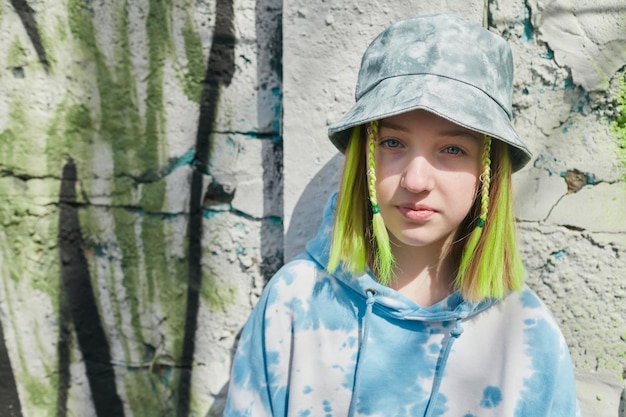 Portrait of young girl with yellow dyed hairstyle in hat looking at camera standing outdoors