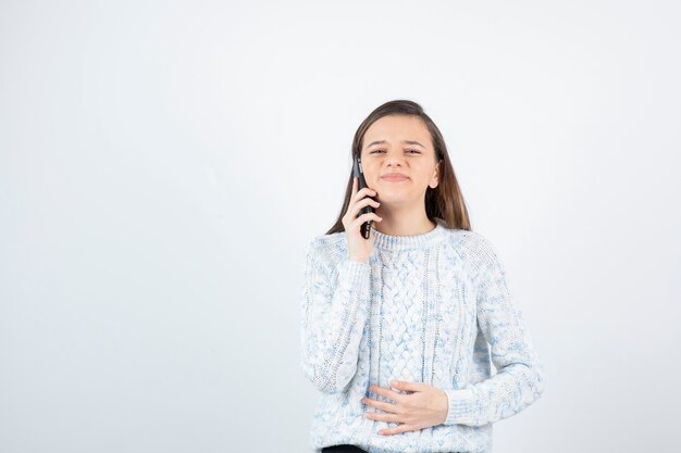 Portrait of young girl in wool sweater talking with someone over cellphone.