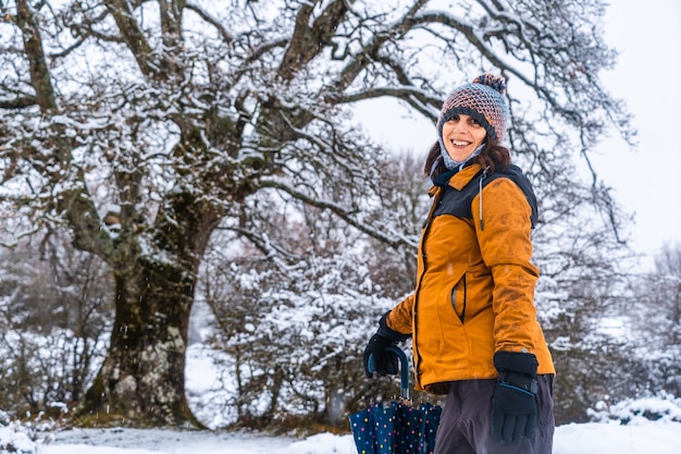 Portrait of a young girl in a yellow jacket next to a giant snowy tree. Snow in the town of Opakua near Vitoria in Araba