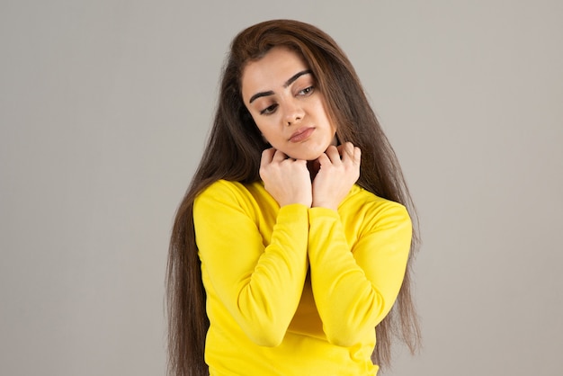 Portrait of young girl in yellow top looking and looking on gray wall.