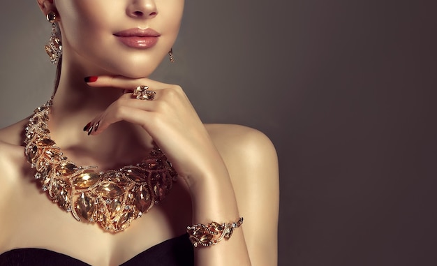 Портрет молодой великолепной женщины, одетой в комплект ювелирных изделий из ожерелья, кольца, браслета и серег. Симпатичная голубоглазая модель демонстрирует привлекательный макияж и маникюр.