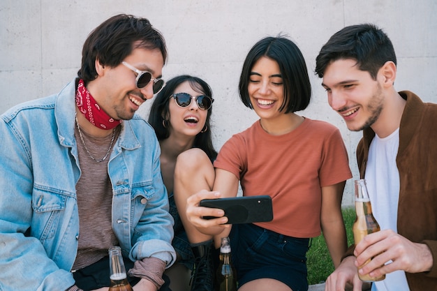 Portrait of young group of friends spending time together while watching something in smartphone outdoors. Technology and friendship concept.