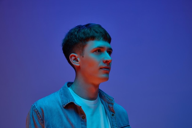 Portrait of young guy in casual clothes posing looking away with calm face against gradient purple