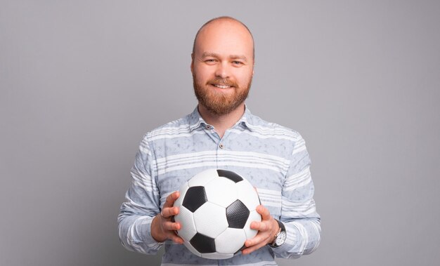 Portrait of young guy in casual holding soccer ball and looking at the camera