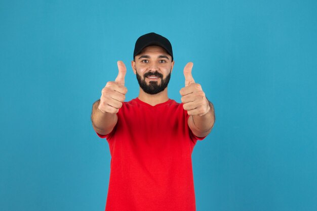 Portrait of a young guy making a thumb up sign against blue wall . 