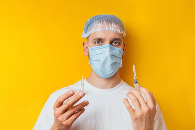 Portrait of a young guy in a respirator on a yellow background Holding an ampoule with a coronavirus vaccine Cold medicine The concept of coronavirus