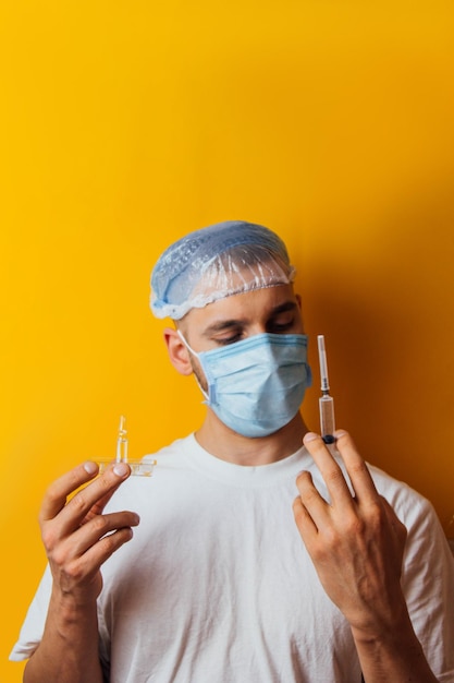 노란색 배경에 호흡기를 착용한 젊은 남자의 초상화 코로나바이러스 백신으로 앰플을 들고 감기약 코로나바이러스의 개념