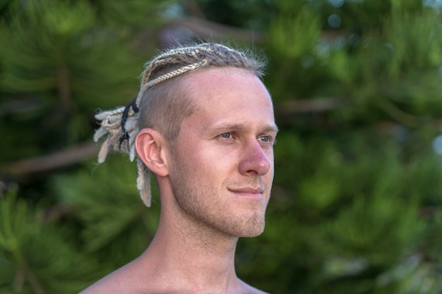 自然の中で彼の頭にドレッドヘアを持つ若い男の肖像画。熱帯のビーチでドレッドヘアを持つ幸せなハンサムな男、クローズアップ