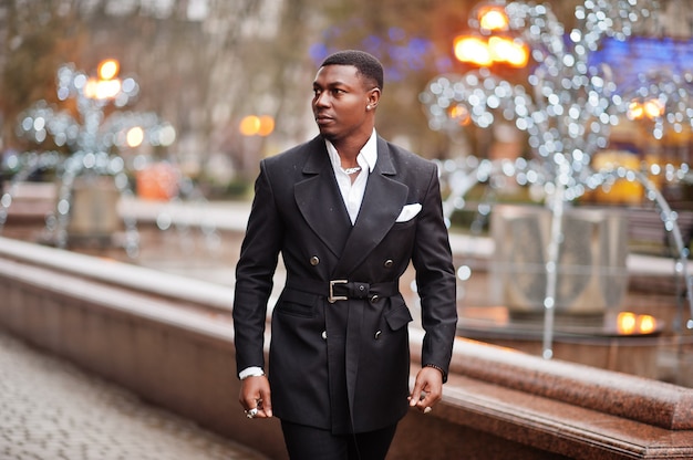 Portrait of young and handsome african american businessman in suit walking on cemter of city with garlands.