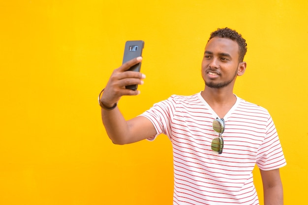 Portrait of young handsome African bearded man with Afro hair against yellow wall in the streets outdoors