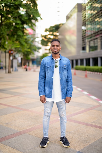 Portrait of young handsome African bearded man with Afro hair exploring the city streets outdoors