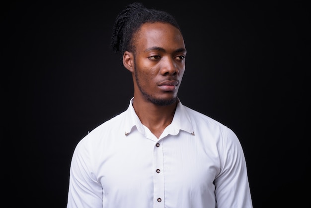 portrait of young handsome African businessman with dreadlocks on black