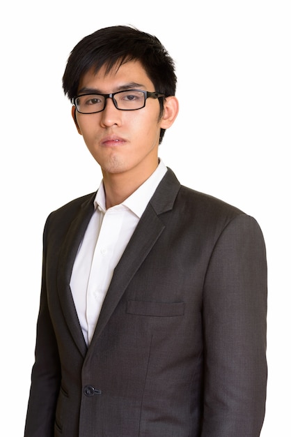 白い壁に対して隔離されたスーツの若いハンサムなアジアのビジネスマンの肖像画