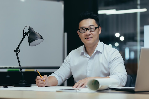 Портрет молодого красивого азиатского архитектора-дизайнера-фрилансера, сидящего в офисе в